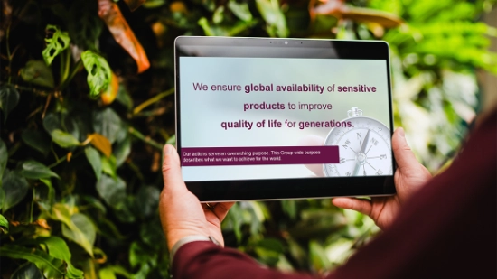 A tablet showing the Uhlmann Group purpose held in front of a green plant wall.