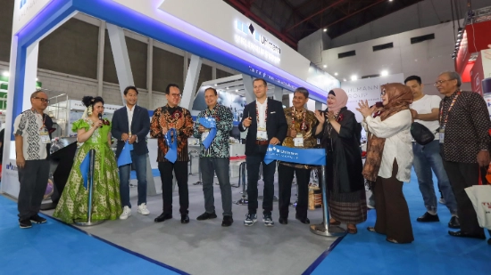 People standing in front of a trade fair booth applauding while a ribbon is symbolically cut to mark the opening of the new branch