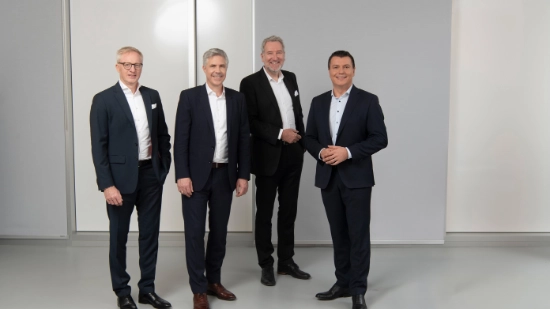 Uhlmann management team: Alexander Schöllhorn, Prof. Dr.-Ing. Matthias Niemeyer, Cristian Reiter and Michael Mrachacz smiling in front of a machine in a hall.
