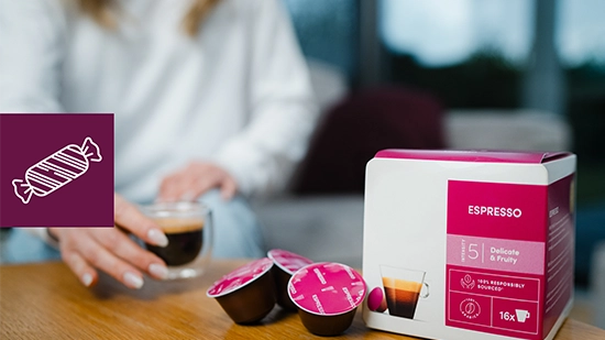 Coffee capsules, coffee packaging, and a cup placed on a table. An icon on the image represents food products.