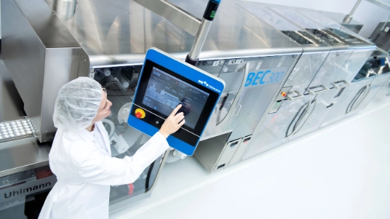 Uhlmann employee wearing protective clothing operating an Uhlmann packaging machine via a touchscreen