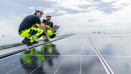 Two technicians inspect solar panels on a large outdoor photovoltaic installation.