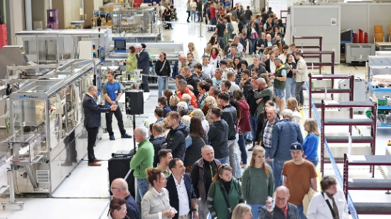 View into an industrial hall: Many people move around the hall on a course and look at machines.