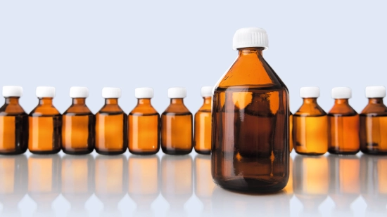 A row of brown glass bottles filled with liquid. There is one bottle by itself in the foreground.