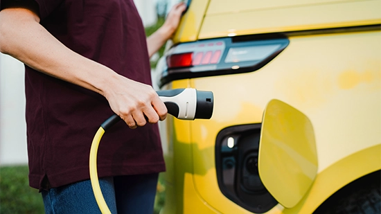 A person charges an electric car using a charging cable at a charging station