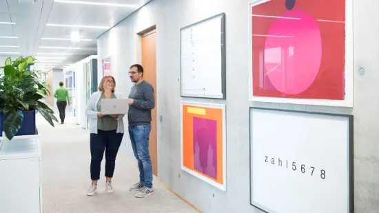 Two employees standing with a laptop in a bright office corridor featuring modern artwork