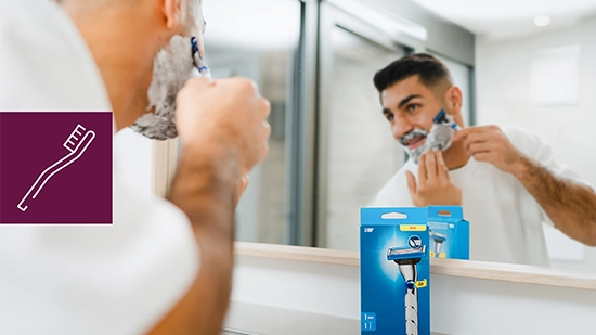 Male person shaving in front of a bathroom mirror using a razor. An icon on the image symbolizes a toothbrush, representing everyday consumer products.
