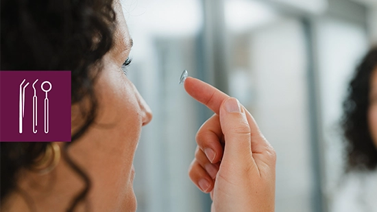 Female person holding a contact lens close to the eye in front of a mirror. An icon on the image shows medical instruments representing healthcare.
