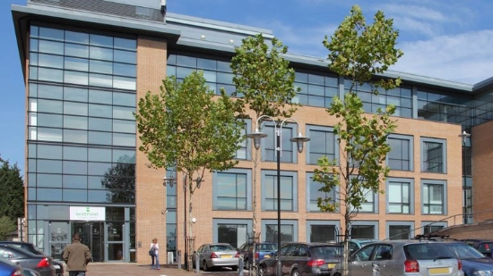 Uhlmann UK Ltd. Edificio corporativo con arbustos verdes y un árbol en un aparcamiento bajo un cielo azul