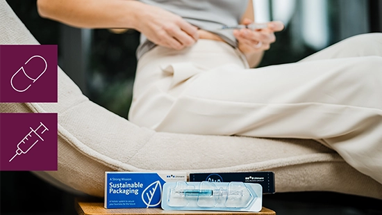 Pharmaceutical product packaging placed in front of a sofa next to a seated person with a needle in their hand. On the picture are two icons symbolizing a pill and syringe.
