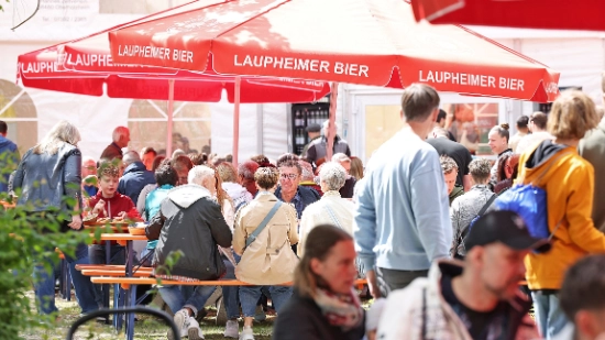 Lots of people sitting under red parasols in a relaxed atmosphere in the Uhlmann beer garden