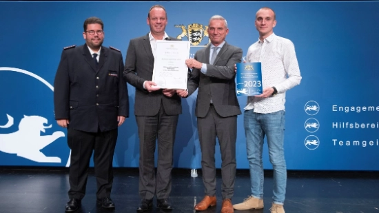 Four people standing on a stage holding a certificate and an award plaque