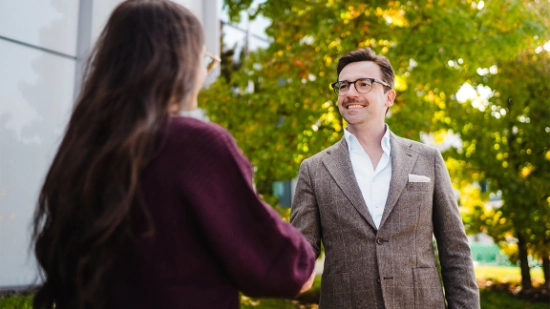 Two people shaking hands in front of a company building.