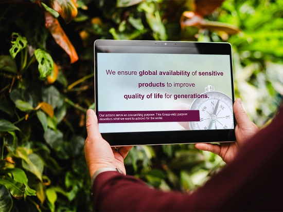 A tablet showing the Uhlmann Group purpose held in front of a green plant wall.