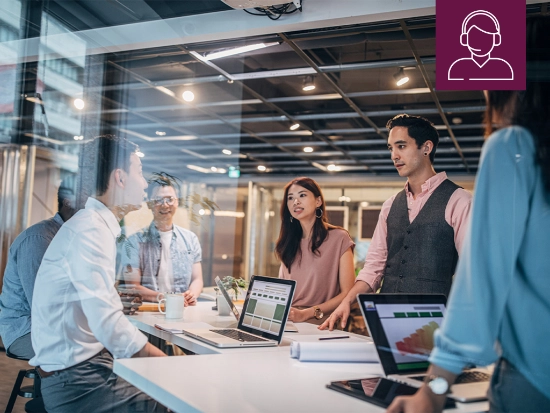 Employees collaborating at a shared workspace with laptops and documents in a modern office environment. An icon on the image represents centralized support services.