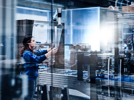 A woman is standing in a production hall in front of a large packaging machine.
