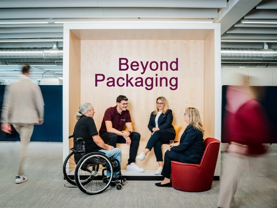 Group of people sitting in a modern office lounge with the words “Beyond Packaging” in the background.