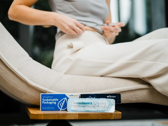 Person sitting on a chair is holding a syringe towards her stomach.