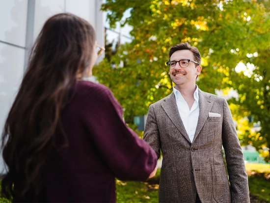 Two people shaking hands in front of a company building.