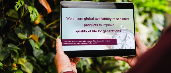 A tablet showing the Uhlmann Group purpose held in front of a green plant wall.
