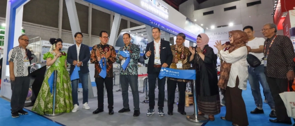 Vor einem Messestand stehen Menschen und applaudieren, während symbolisch ein Band durchschnitten wird, um die Eröffnung zu feiern.