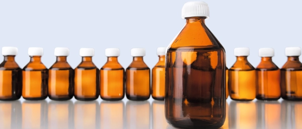 A row of brown glass bottles filled with liquid. There is one bottle by itself in the foreground.
