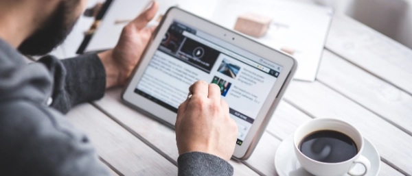 A person sitting at a table and holding a tablet that shows online news articles.