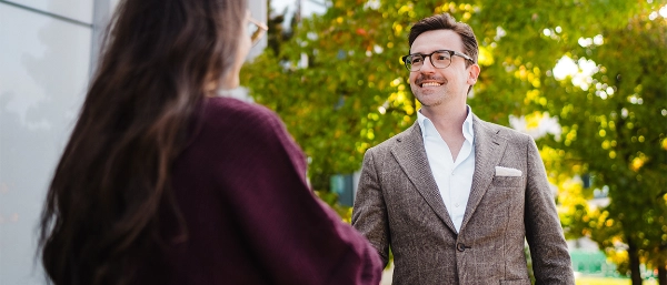 Two people shaking hands in front of a company building.