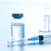 Primer plano de una jeringuilla, ampollas y un vial con líquido transparente.